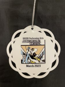 Image of the ornament for sale with On the Twentieth Century logo and March 2023 printed on the front. The ornament is a white circle with radial lines around the edge.